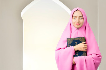 Asian Muslim woman in a veil standing and holding the Quran