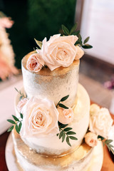 wedding cake three tiers floors white gold with flowers roses and stand on a dark background
