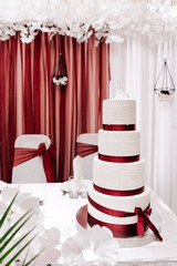 Fototapeta na wymiar wedding cake white cream mastic four floors with red ribbons and bow with newlyweds from above on a white background