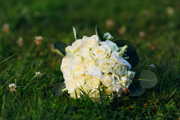 Obraz na płótnie Canvas A wedding bouquet of white roses lies on the green grass