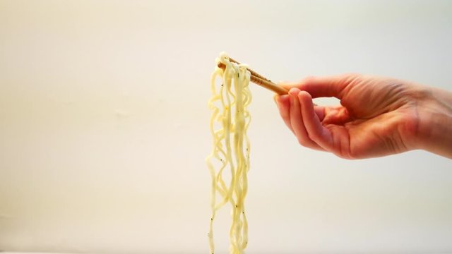 Hand of young woman gets instant noodles in cup on the table while using chopsticks on a white background stock video
