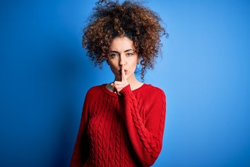Fototapeta na wymiar Young beautiful woman with curly hair and piercing wearing casual red sweater asking to be quiet with finger on lips. Silence and secret concept.