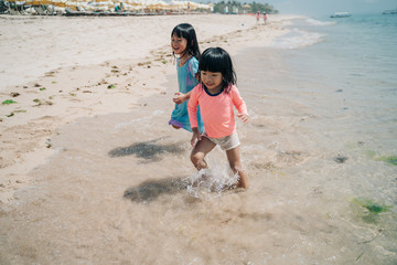 two little Asian girl running to avoid the waves, playing on the beach enjoying the pleasure of vacationing