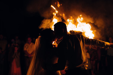 newlyweds kissing at night against the background of fire and gu