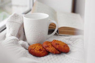 a Cup of tea with oatmeal cookies is on the window, a knitted sweater, an old Flat lay book