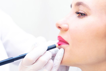 Young woman having permanent makeup on her lips at the beauticians salon. Permanent Makeup (Tattoo). drawing a contour with a white lip pencil