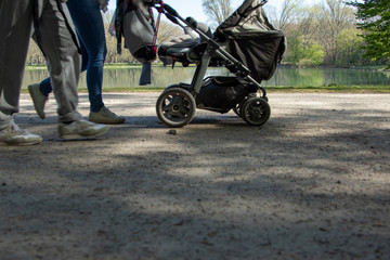 legs of people and a stroller buggie in the park, lake as background