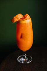 Garibaldi cocktail decorated with mandarin orange zest. Dark green color wall as background.