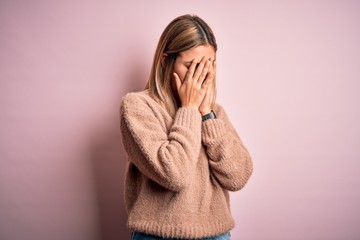 Young beautiful blonde woman wearing winter wool sweater over pink isolated background with sad expression covering face with hands while crying. Depression concept.