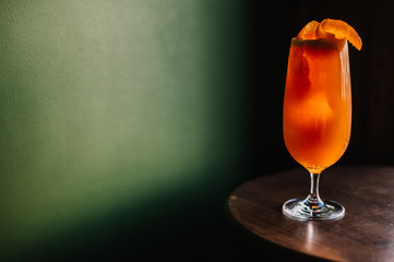 Garibaldi cocktail decorated with mandarin orange zest. Dark green color wall as background.