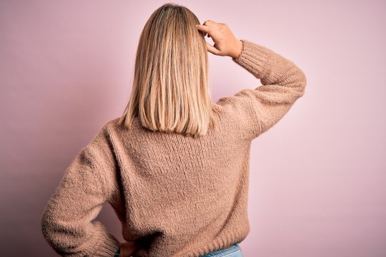 Young beautiful blonde woman wearing winter wool sweater over pink isolated background Backwards thinking about doubt with hand on head