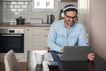 Businessman listening music on headset while working on laptop.