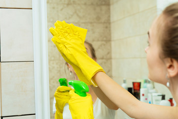 A girl is washing a mirror in yellow gloves. A girl is cleaning a mirror with detergents