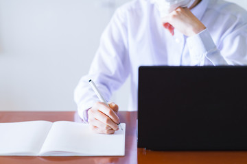 Japanese business person writing on notebook and using laptop computer at home