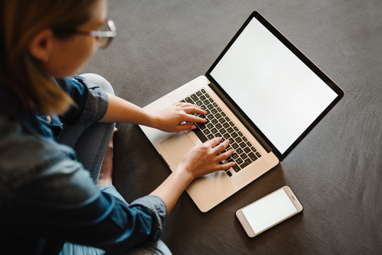 Beautiful happy young woman working and using white blank screen laptop computer in the bedroom. Freelancer. Writing, typing. Communication and technology concept. Blank screen smartphone. Top view.