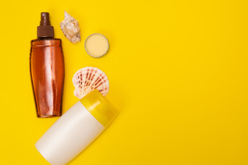 A suncream with shells are on the yellow background. Sun protection products are on the yellow background in close view.
