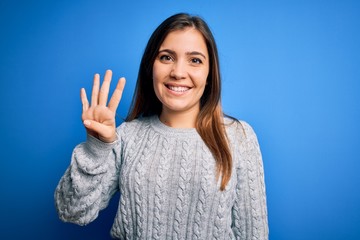 Beautiful young woman wearing casual wool sweater standing over blue isolated background showing and pointing up with fingers number four while smiling confident and happy.