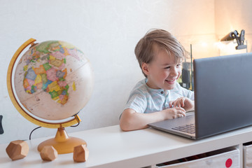 A boy toddler is studying geography an online lesson with a globe and a world map sitting at home...