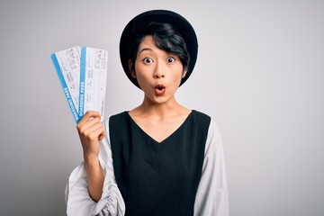 Young beautiful chinese tourist woman holding boarding pass airlane over white background scared in...