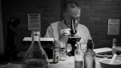In black and white a scientist during the 1918 influenza pandemic working in his private laboratory searching for a cure to the Spanish Flu. - obrazy, fototapety, plakaty