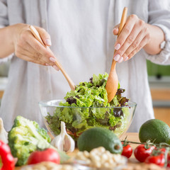 Woman cooking healthy food in the kitchen and mixing fresh salad