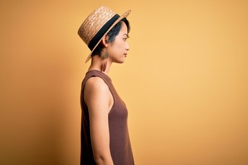 Young beautiful asian girl wearing casual t-shirt and hat over isolated yellow background looking...
