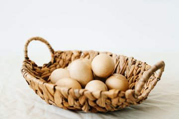 a natural basket with Easter eggs in a pastel brown color and with cracks stands on a white table.Easter concept.Minimal style. copy space for text