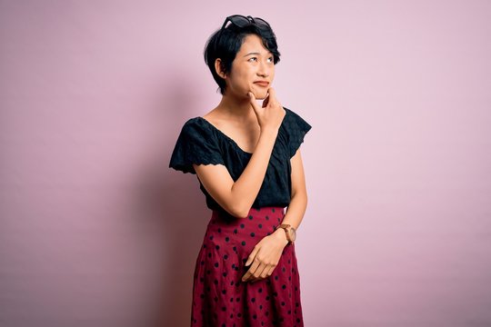 Young beautiful asian girl wearing casual dress standing over isolated pink background Thinking worried about a question, concerned and nervous with hand on chin