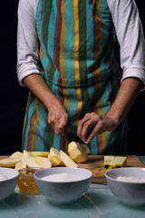 Working in the kitchen. avertical hlf-length photography. Detail of hands cutting apple into pieces. Black background.