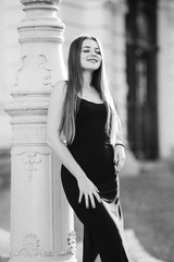 girl with long hair in a black dress poses near the column on bl