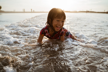 Asian little girl sitting on sand in the beach while playing water on a nice beach