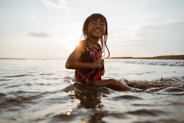 Asian little girl sitting on sand in the beach while playing water on a nice beach