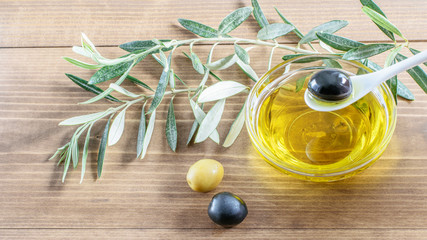Olive in spoon over the glass transparent bowl with olive oil on the wooden background. Healthy...