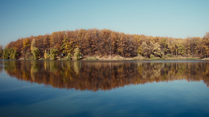 Autumn landscape, yellow trees are reflected on the surface of the lake.