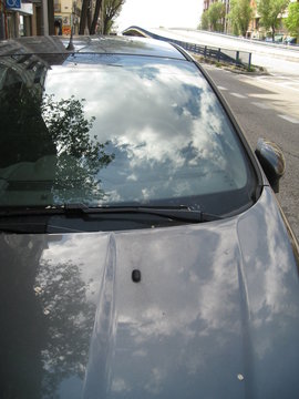 coche azul con reflejo de nubes y &aacute;rboles en cristal delantero y en cap&oacute;