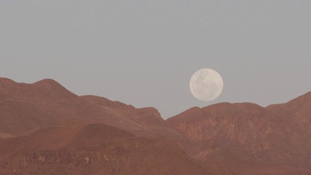 Moonrise at dusk over desert mountains.