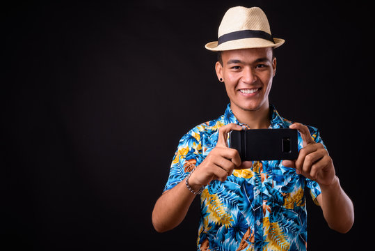 Portrait of happy young Indian tourist man taking picture with phone