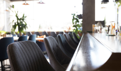 Long blurred table with chairs near bar with alcohol drinks