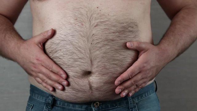 shirtless caucasian fat man slams and knocks by hands himself on the big belly which shakes like a drum