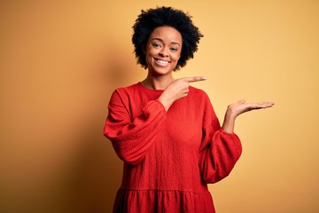 Young beautiful African American afro woman with curly hair wearing casual sweater amazed and smiling to the camera while presenting with hand and pointing with finger.