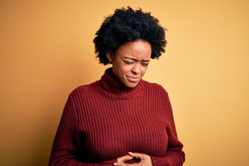 Young beautiful African American afro woman with curly hair wearing casual turtleneck sweater with hand on stomach because indigestion, painful illness feeling unwell. Ache concept.
