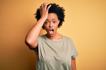 Young beautiful African American afro woman with curly hair wearing casual t-shirt surprised with...