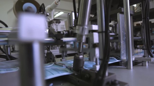 Manufacture of medical masks. Medical mask on conveyor belt in the workshop of factory for production of medical clothing. Production of disposable medical clothing for protection against the virus.