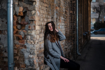 Girl in a red blouse and a gray cardigan on the background of the old brick wall