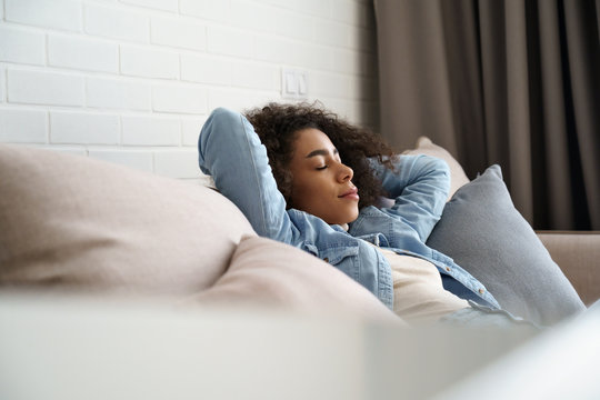 Relaxed tired young african american woman napping on comfortable sofa with eyes shut closed. Calm lazy black girl leaning on couch in living room enjoying chill sleeping resting at home concept.