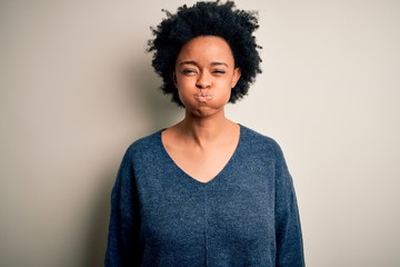 Young beautiful African American afro woman with curly hair wearing casual sweater puffing cheeks with funny face. Mouth inflated with air, crazy expression. - obrazy, fototapety, plakaty