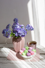 lilac flowers in vase on wooden table, macarons and hydrangea morning light
