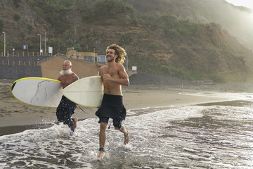Father and son doing surfing in a perfect day. Friends going out into the ocean. Sporty people lifestyle and extreme sport concept - Image