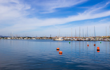 Classic white yachts anchored in the port of Alghero, blue calm sea with red buoys and blue sky with white clouds. Sardinia, Italia.  