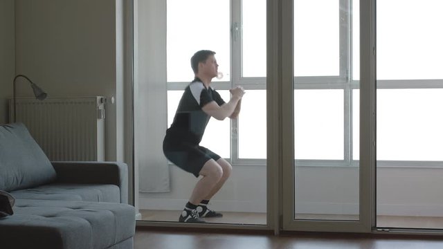 Young man doing squat exercises in the balcony. Home wellness training.